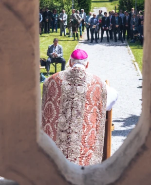 Blick durch eine Zinne auf eine Feldmesse mit vielen Farbstudent:innen.